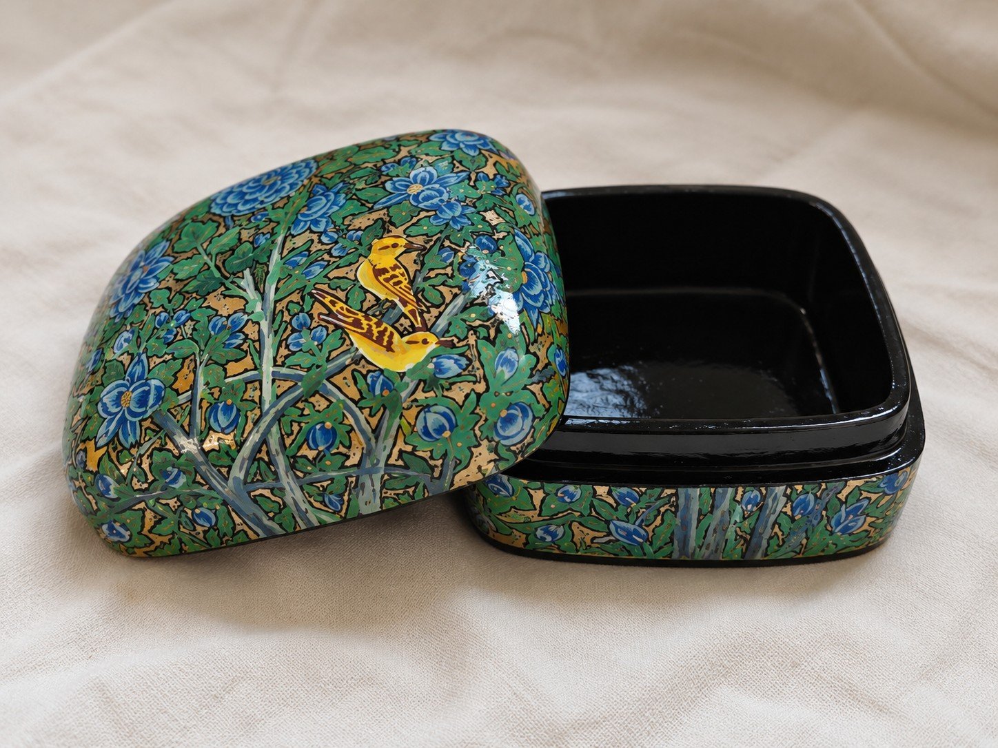 Open green papier mache box with a golden bird on the lid and glossy black lacquered interior