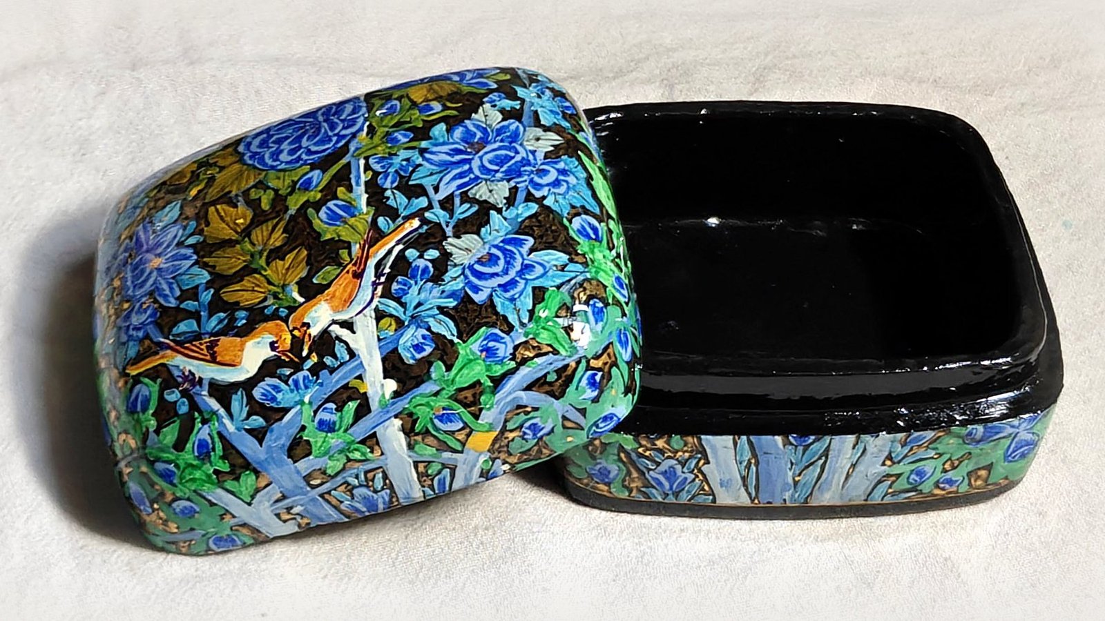 Blue Garden papier mache box No. 1 hand-painted with a songbird feeding its mate among cobalt and sky-blue blossoms with olive leaves, real 24K gold strokes in the background, with the lid off, showing the glossy black lacquered interior